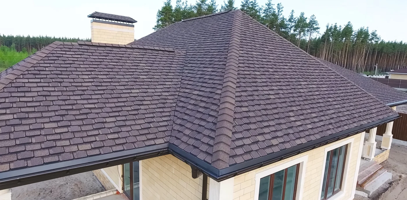 A close drone view of a home with a brand new dark gray slate roofing system, with trees in the background on a cloudy day.