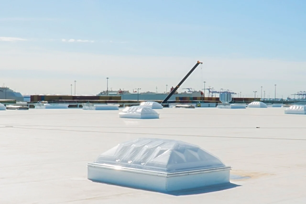 A view of the top of a large industrial building with white roofing and Velux high-performance domes with specialized white laminated glass.