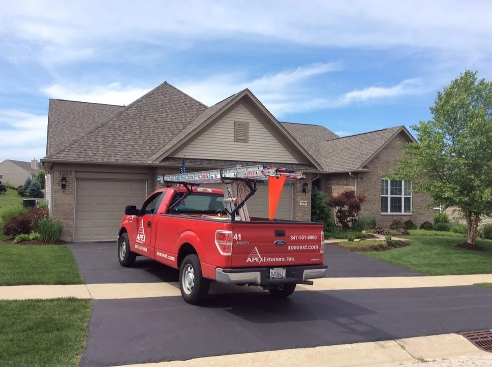 A work truck is parked in front of the house while crews install new gutters.