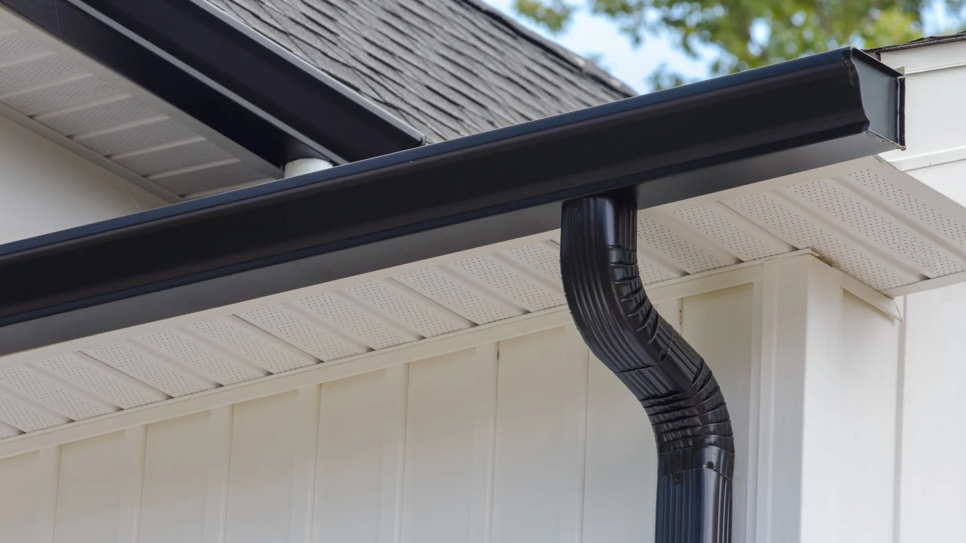 A close-up of a black gutter system on a house with white siding in Buffalo Grove, IL, by Apex Exteriors, Inc.