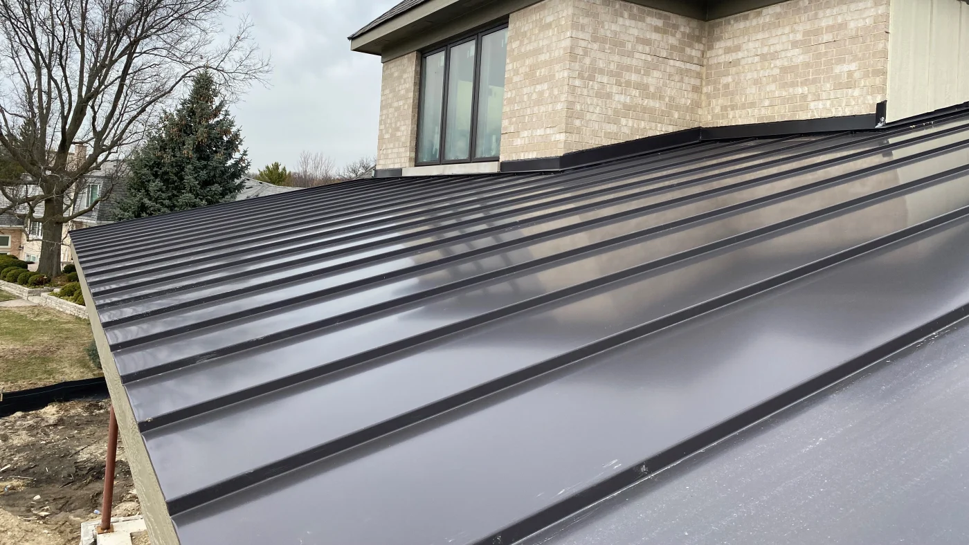 A close-up of a black metal roof on a house with beige siding in Wheaton, IL by Apex Exteriors.