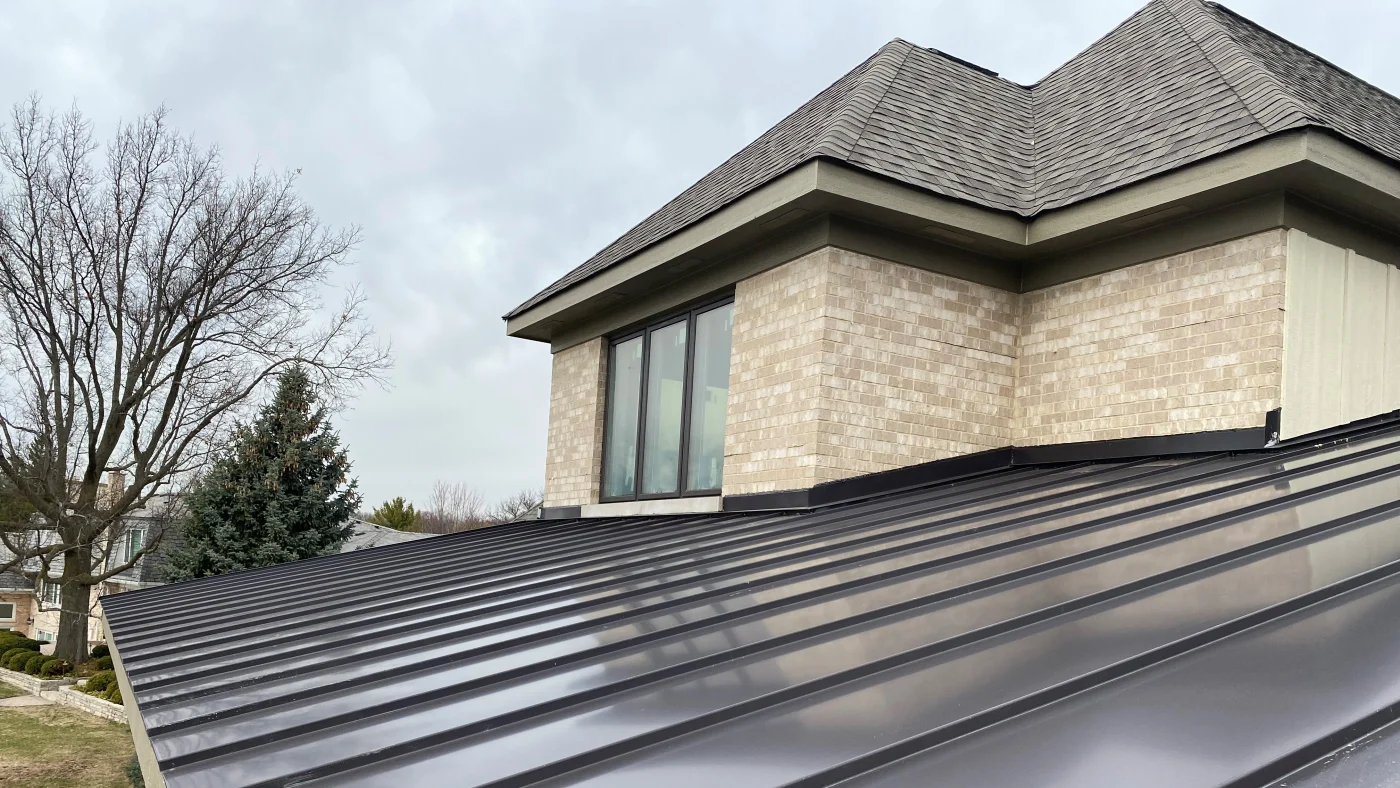 A close-up of a black metal roof on a house with light brown siding in Lombard, IL by Apex Exteriors.