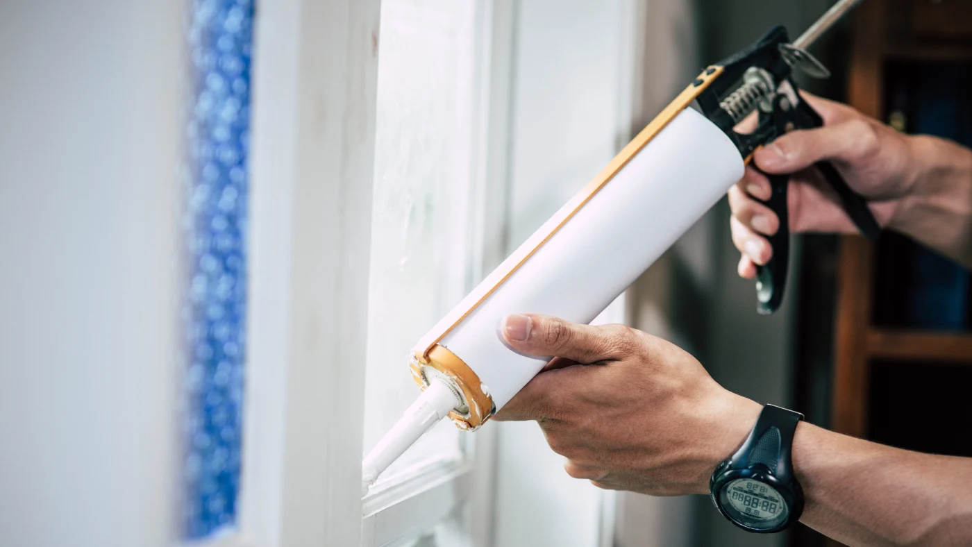 Hands holding a caulk gun sealing a window in Plainfield, IL, by Apex Exteriors, Inc