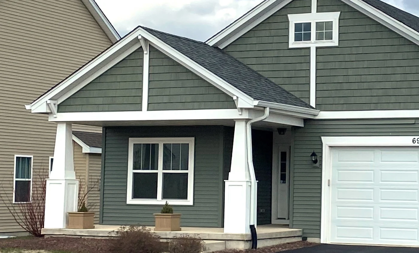 Part of the front of a home with green siding and windows trimmed in white in Wheaton, IL by Apex Exteriors.