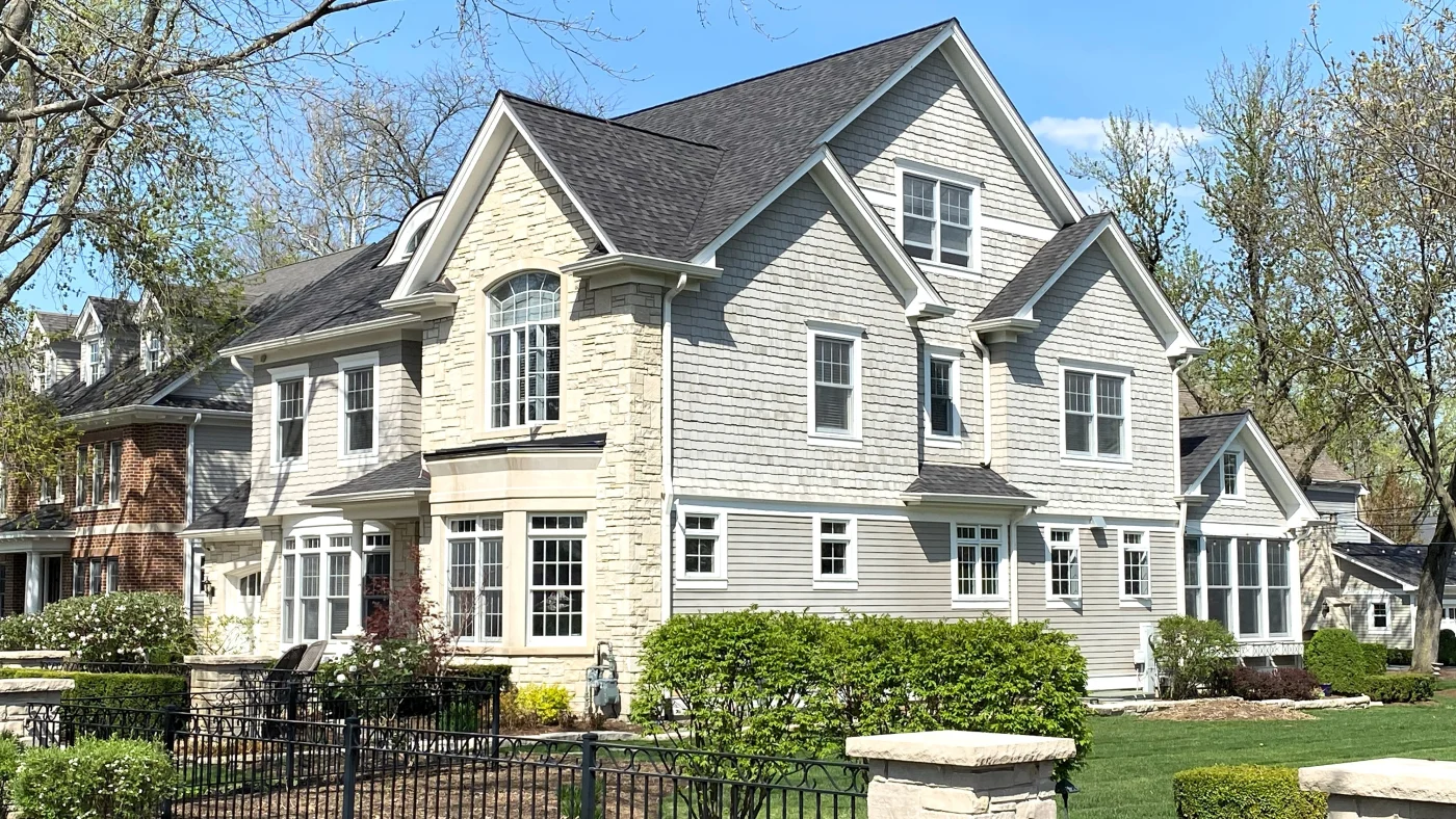 A street view of a large house with white siding and a gray roof in Glenview, IL by Apex Exteriors.