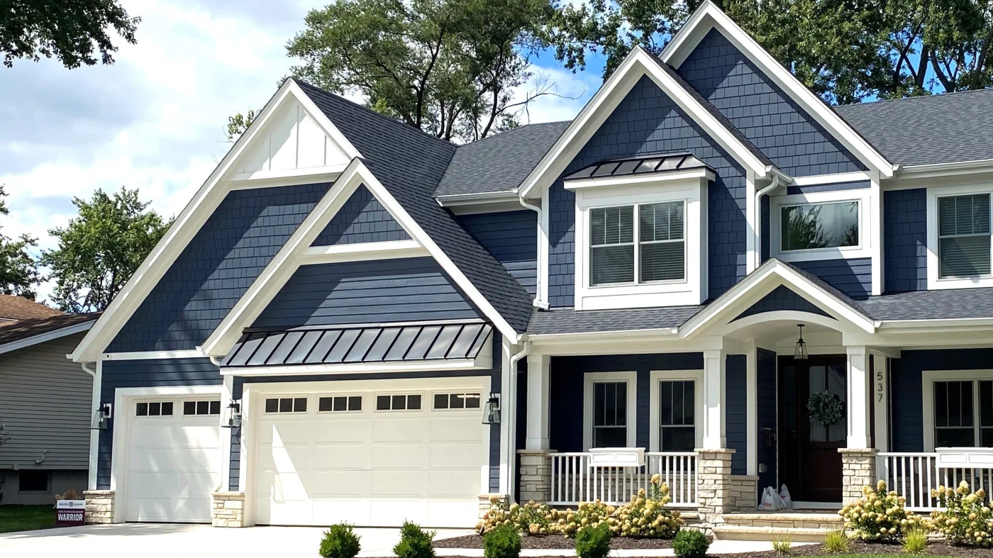 The front of a large house with dark blue siding and white trim in Wheaton, IL by Apex Exteriors.