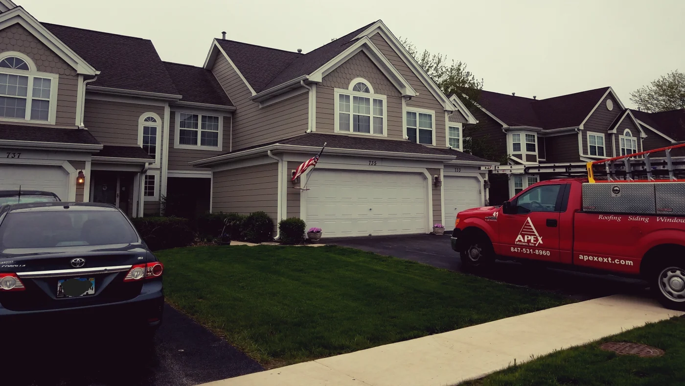 The front of a home in a neighborhood with a company truck parked in the driveway in Elmhurst, IL by Apex Exteriors.