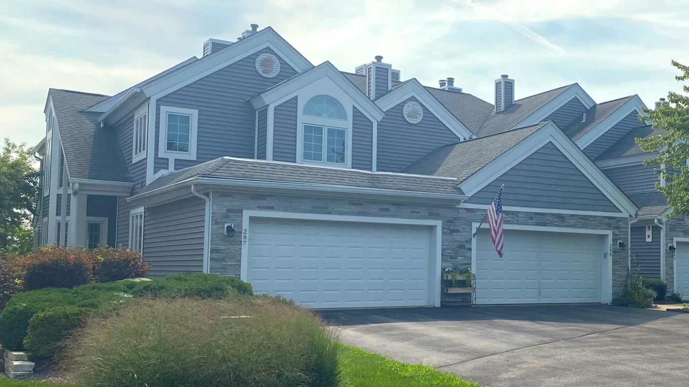 The front of a large house with light brown siding and white trim in Wheaton, IL by Apex Exteriors.