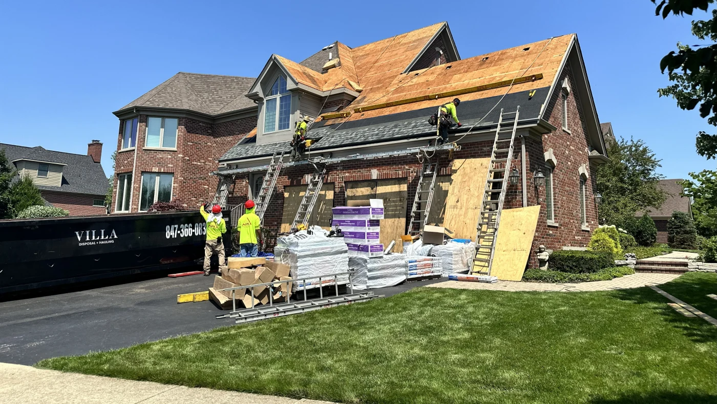 A roofing crew is installing a new roof on a house with brown siding in Wheaton, IL by Apex Exteriors.
