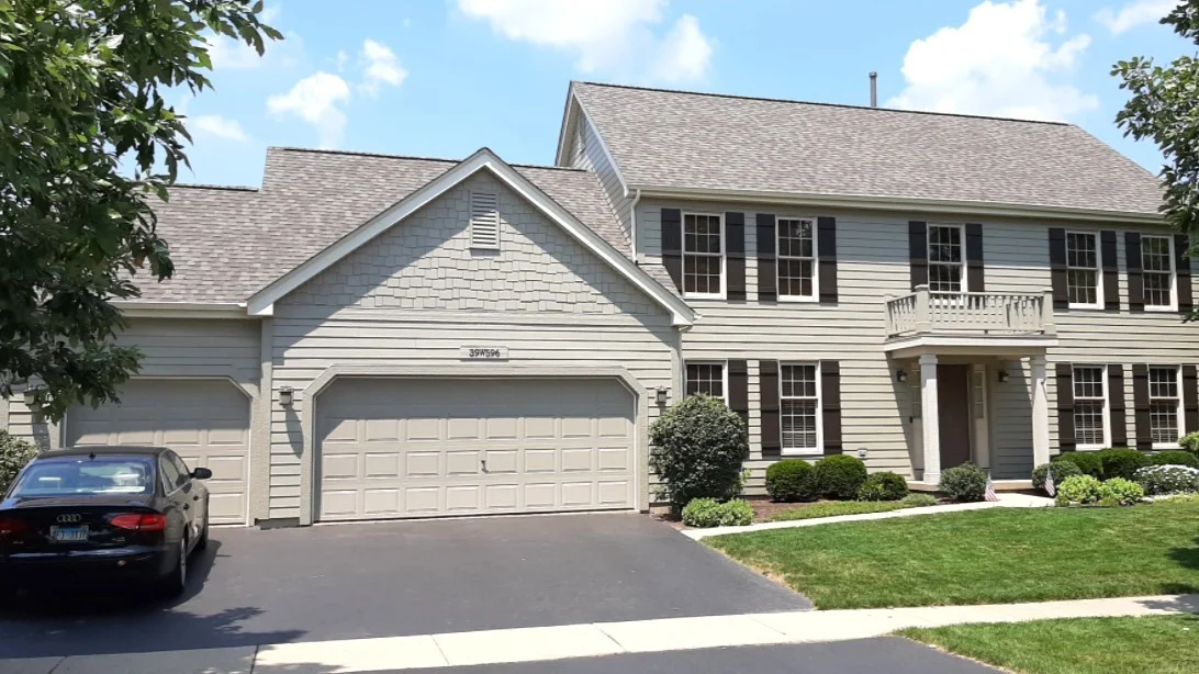 Dependable Roofing Services | Bloomingdale, IL | Apex Exteriors, Inc. The front of a house with light gray siding and a gray roof in Bloomingdale, IL, by Apex Exteriors, Inc.