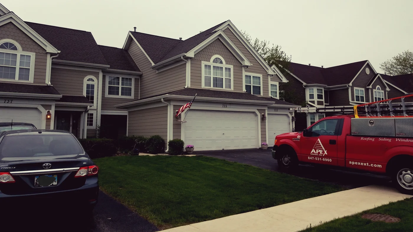 The front of houses on a street with a work truck parked in the driveway of one of them in Elk Grove Village, IL, by Apex Exteriors, Inc.