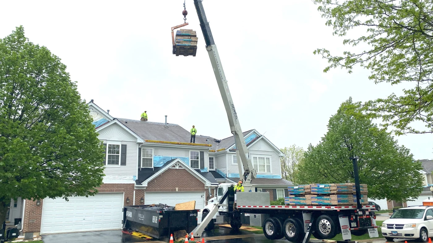 A roofing crew with equipment is installing a new roof on a house in Elk Grove Village, IL, by Apex Exteriors, Inc.