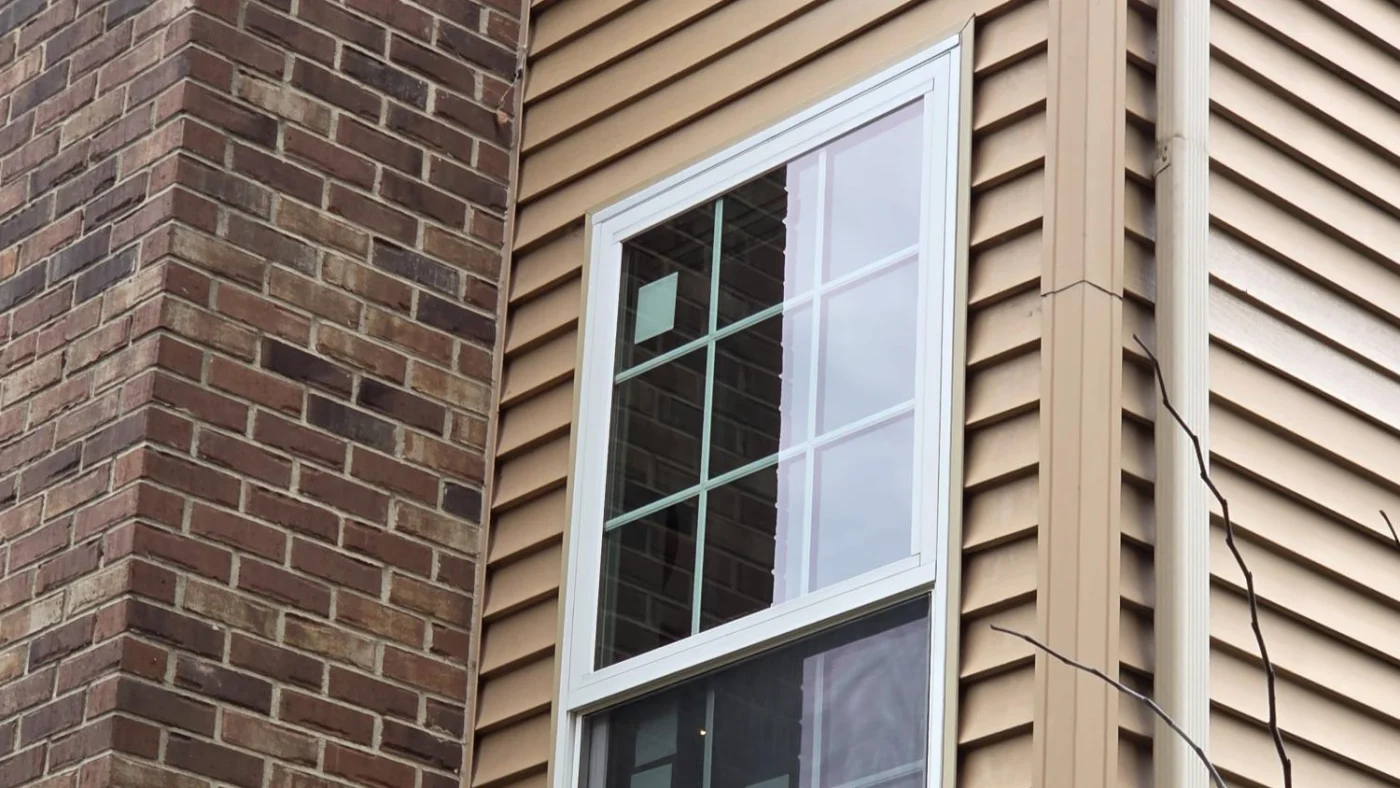 Stunning Residential Window Replacement | Plainfield, IL | Apex Exteriors, Inc. A close-up of the exterior of a home with brown brick and beige vinyl siding in Plainfield, IL, by Apex Exteriors, Inc.