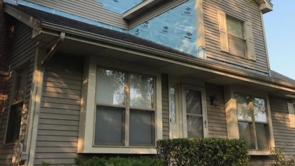 A closer-up view of a house with tan siding undergoing a siding replacement in Glenview, IL, by Apex Exteriors, Inc.