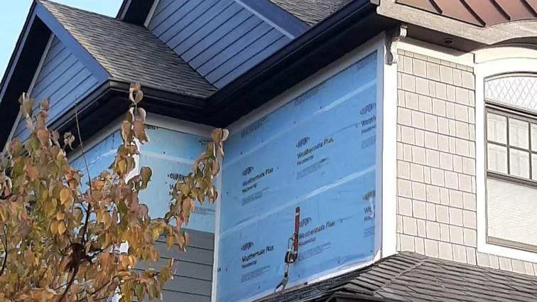 A close-up looking up at a house with light gray siding undergoing a siding replacement in Wheaton, IL, by Apex Exteriors, Inc.