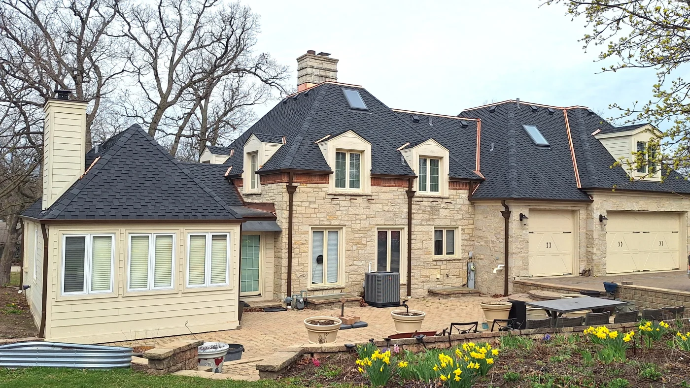 Outstanding Roof Replacement Services | Lombard, IL | Apex Exteriors, Inc. The front of a house with tan siding and a dark gray roof in Lombard, IL, by Apex Exteriors, Inc.