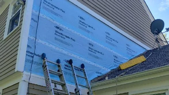 A close-up of the side of a house with tan siding with white trim undergoing a siding replacement in Bloomingdale, IL, by Apex Exteriors, Inc.