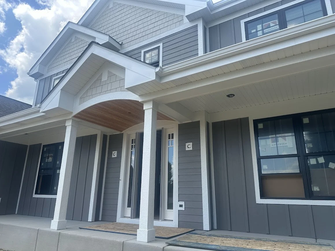 Astounding Window And Door Installation | Plainfield, IL | Apex Exteriors Modern two-story home with gray vertical siding, white trim, covered front porch, and newly installed black-framed windows and glass entry doors.