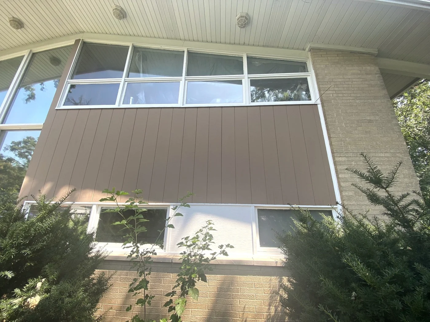 Close-up of a mid-century modern home showing replacement windows with brown vertical siding over a brick wall.