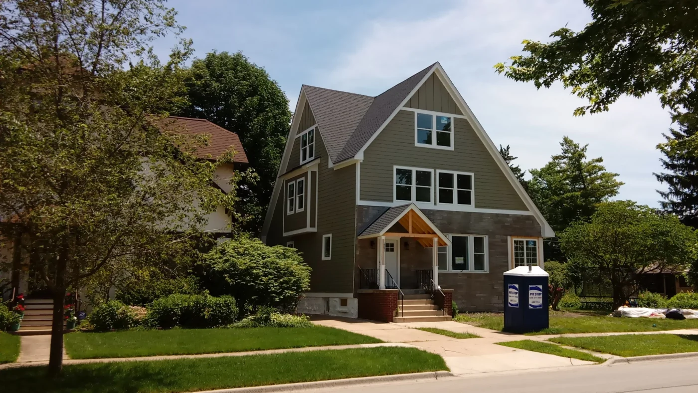 The front of a house from across a street with green siding and multiple windows trimmed in white in Elmhurst, IL, by Apex Exteriors, Inc.