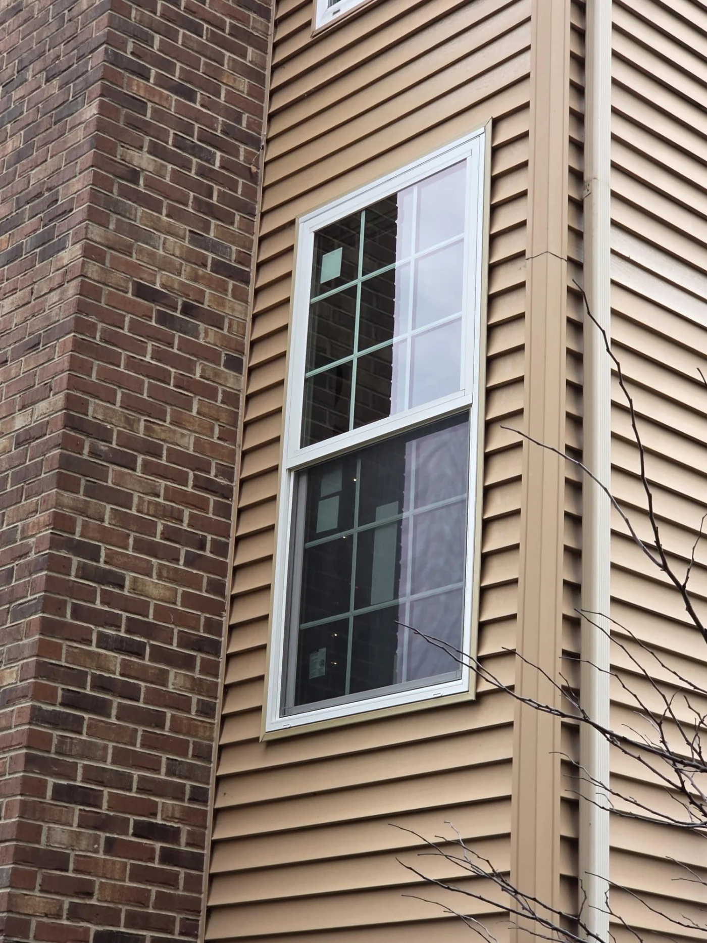 Stupendous Window And Door Installation | Plainfield, IL | Apex Exteriors Front view of a Tudor-style home with brown shingle roof, two dormer windows, stone and wood exterior, and trimmed hedges.