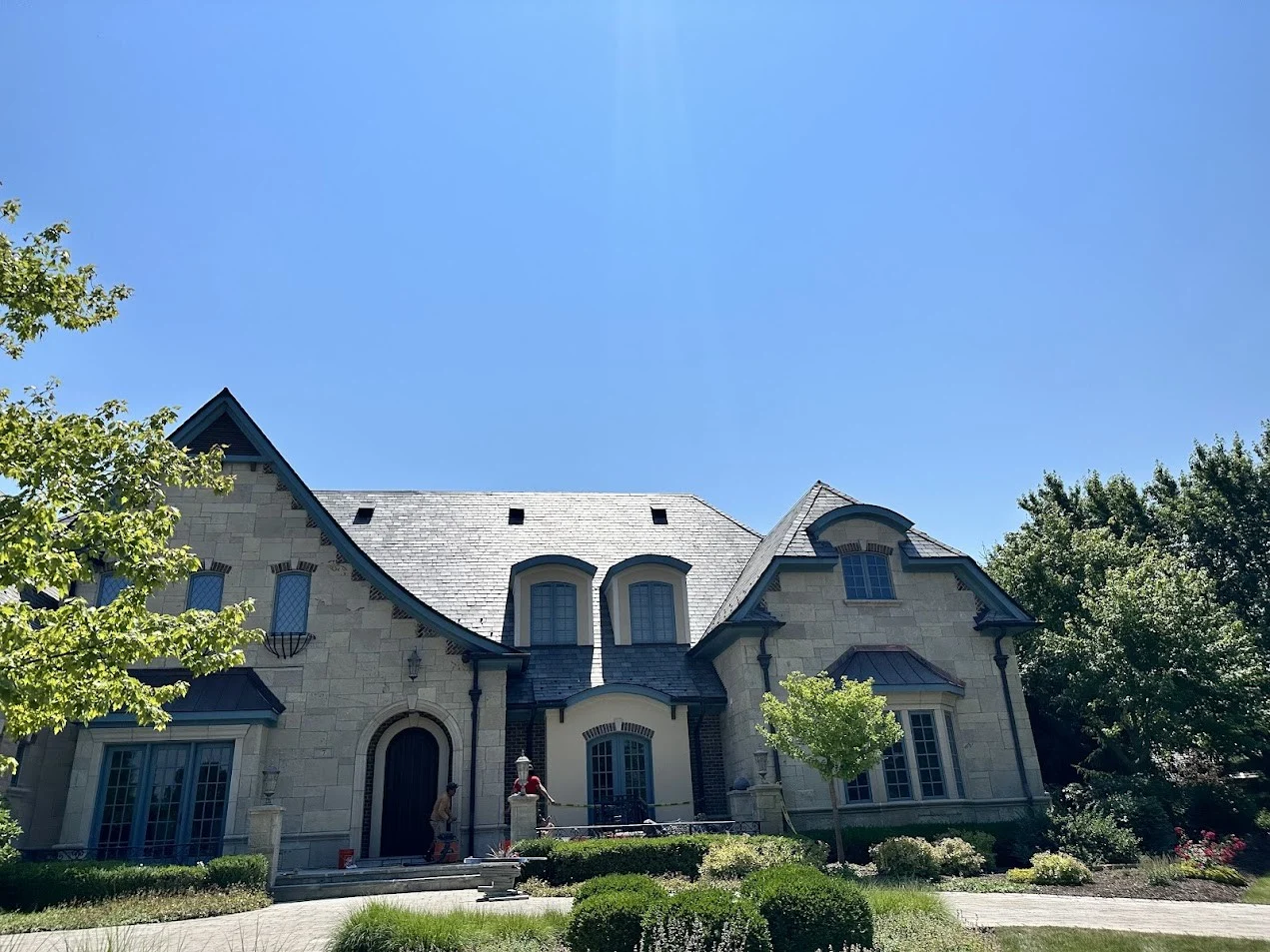 An image of a luxury stone home with elegant slate roofing, steep rooflines, and dormer windows.