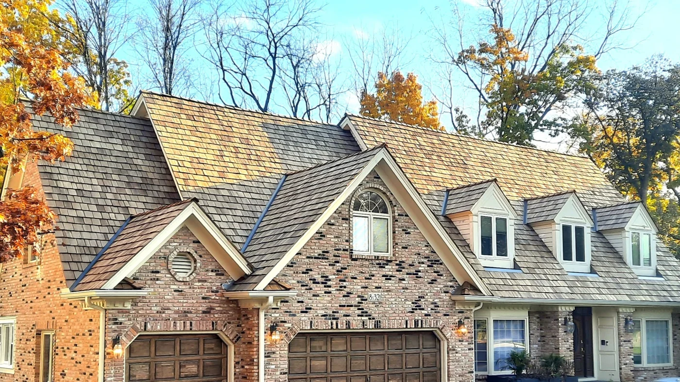 Dependable HOA Exterior Services | Wayne, IL | Apex Exteriors Inc. Brick townhouse-style home with a steep cedar shake roof, dormer windows, and matching garage doors, set among mature trees with autumn foliage.