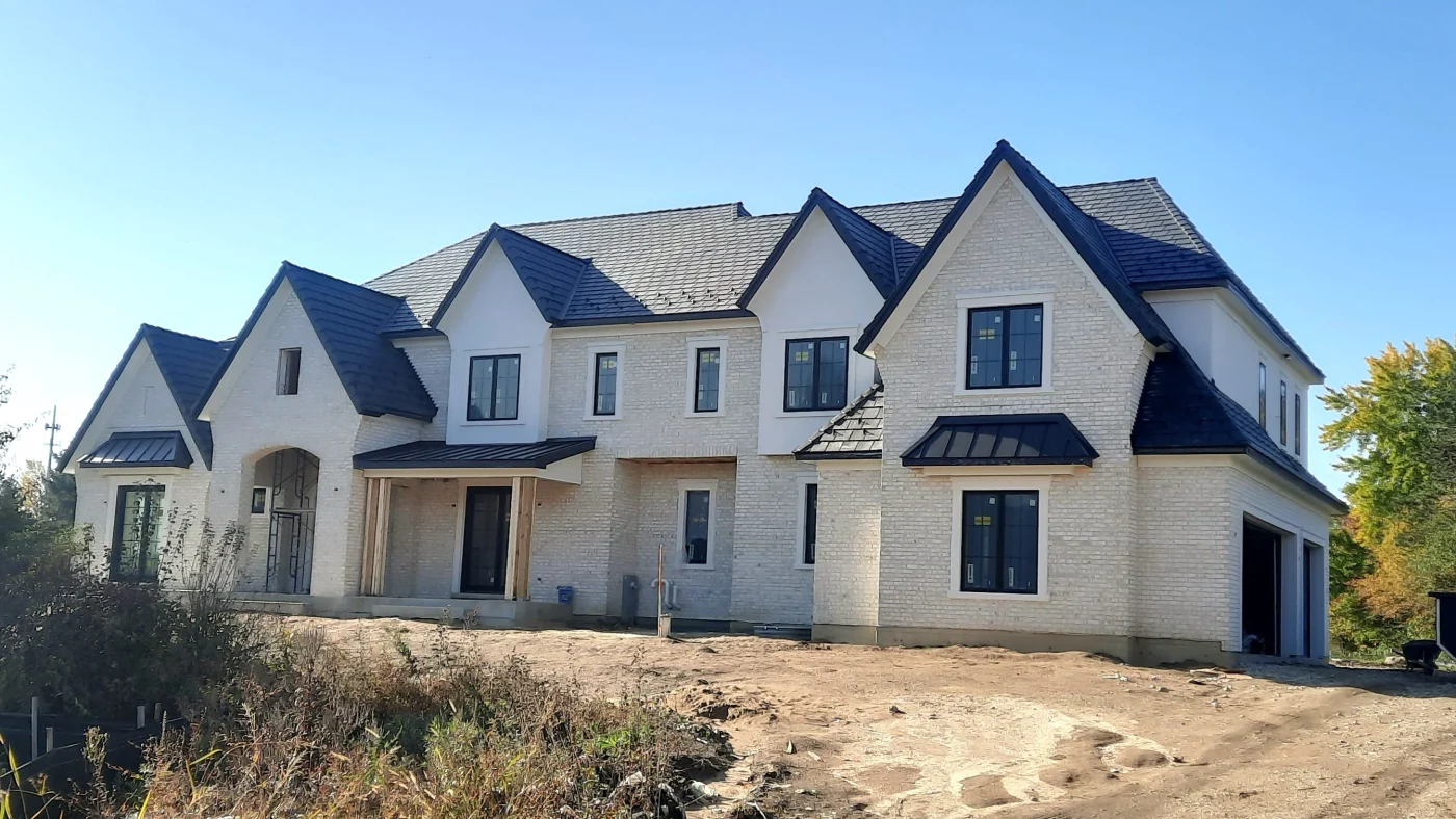 Dependable New Home Construction | Wayne, IL | Apex Exteriors Inc. Large newly constructed home with white brick exterior and dark roof accents, featuring multiple steep rooflines, black-framed windows, and a spacious front elevation set on a graded lot under a clear blue sky.