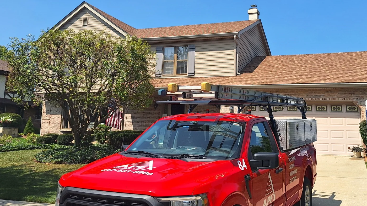 Dependable Roofing Contractor | Wayne, IL | Apex Exteriors Inc. Apex Exteriors service truck is parked in front of a two-story suburban home with a shingle roof, brick and siding exterior, and a well-kept front yard with mature landscaping.