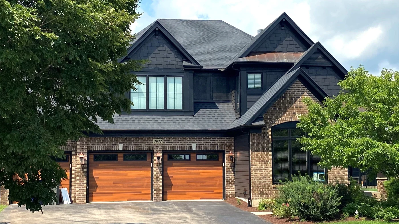 Dependable Siding Contractor | Wayne, IL | Apex Exteriors Inc. High-end exterior upgrade featuring dark siding, brick accents, and custom wood garage doors, creating a bold, modern look with durable, weather-resistant materials.