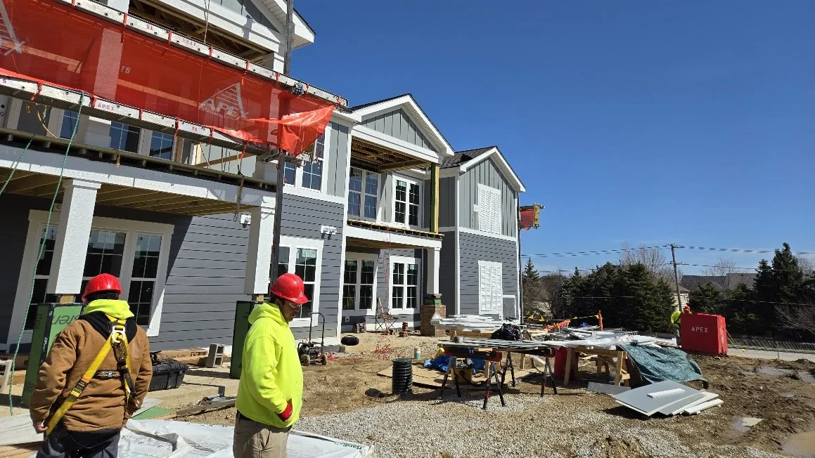 Exceptional Commercial Roofing Contractor | Bartlett, IL | Apex Exteriors, Inc. Aerial view of a large residential development under construction, featuring newly installed roofing, active lift equipment, and a covered entry structure taking shape at the center of the project.