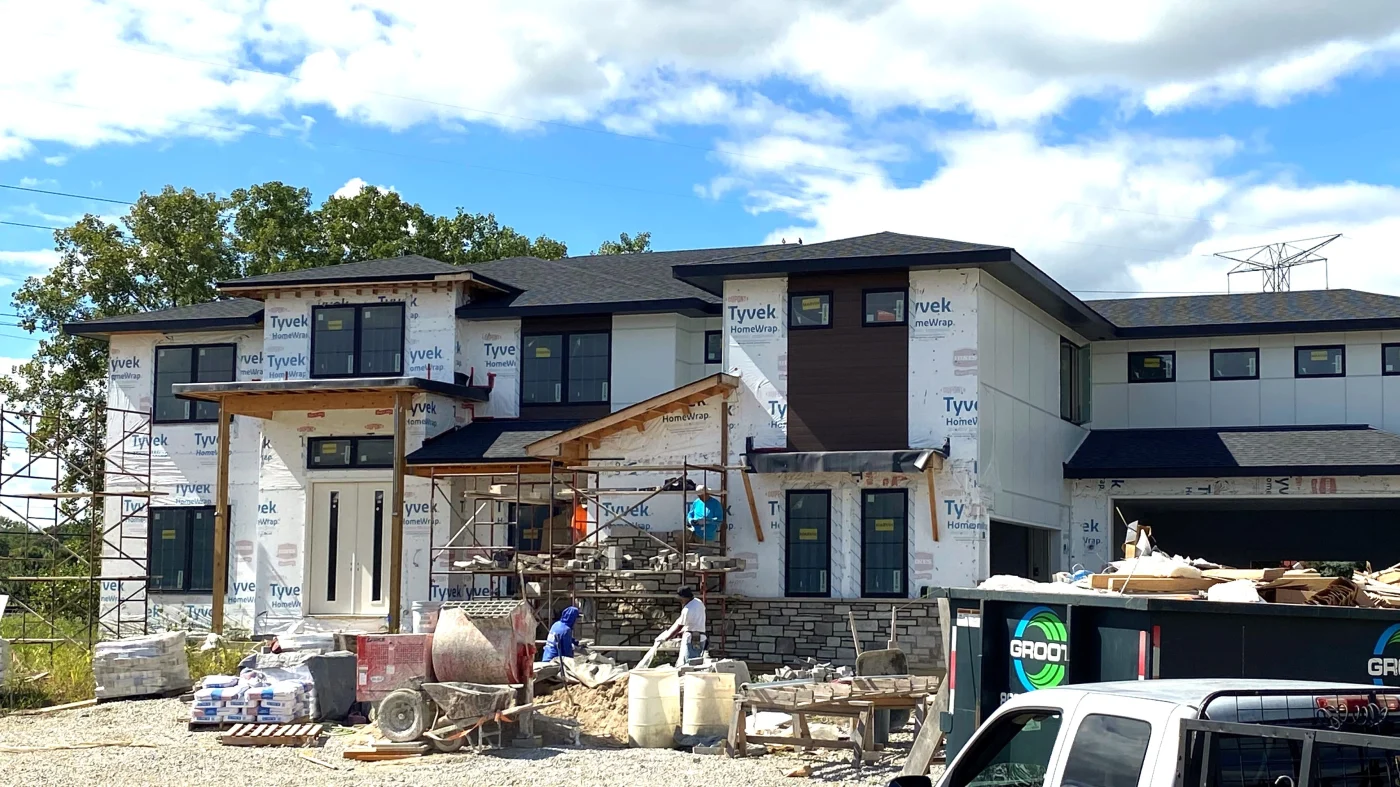 Reliable New Home Construction | Bartlett, IL | Apex Exteriors, Inc. New home under construction wrapped in Tyvek, featuring a dimensional shingle roof and framed openings, with an Apex Exteriors truck on-site highlighting active exterior installation work.