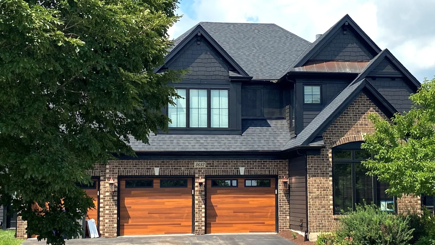 Expert HOA Exterior Services | Wayne, IL | Apex Exteriors Inc. Modern home exterior with dark siding, brick façade, and rich wood garage doors, combining clean lines, durable materials, and strong curb appeal in a polished, HOA-friendly design.