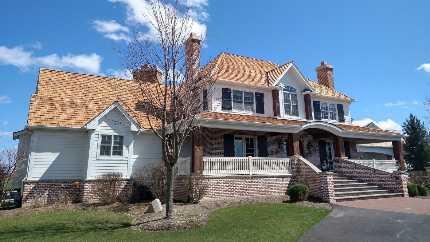 Masterful Roofing Contractor | Wayne, IL | Apex Exteriors Inc. Large two-story home with a newly installed cedar shake roof, highlighting warm natural tones, steep roof pitches, and detailed architectural features, including dormers and chimneys.