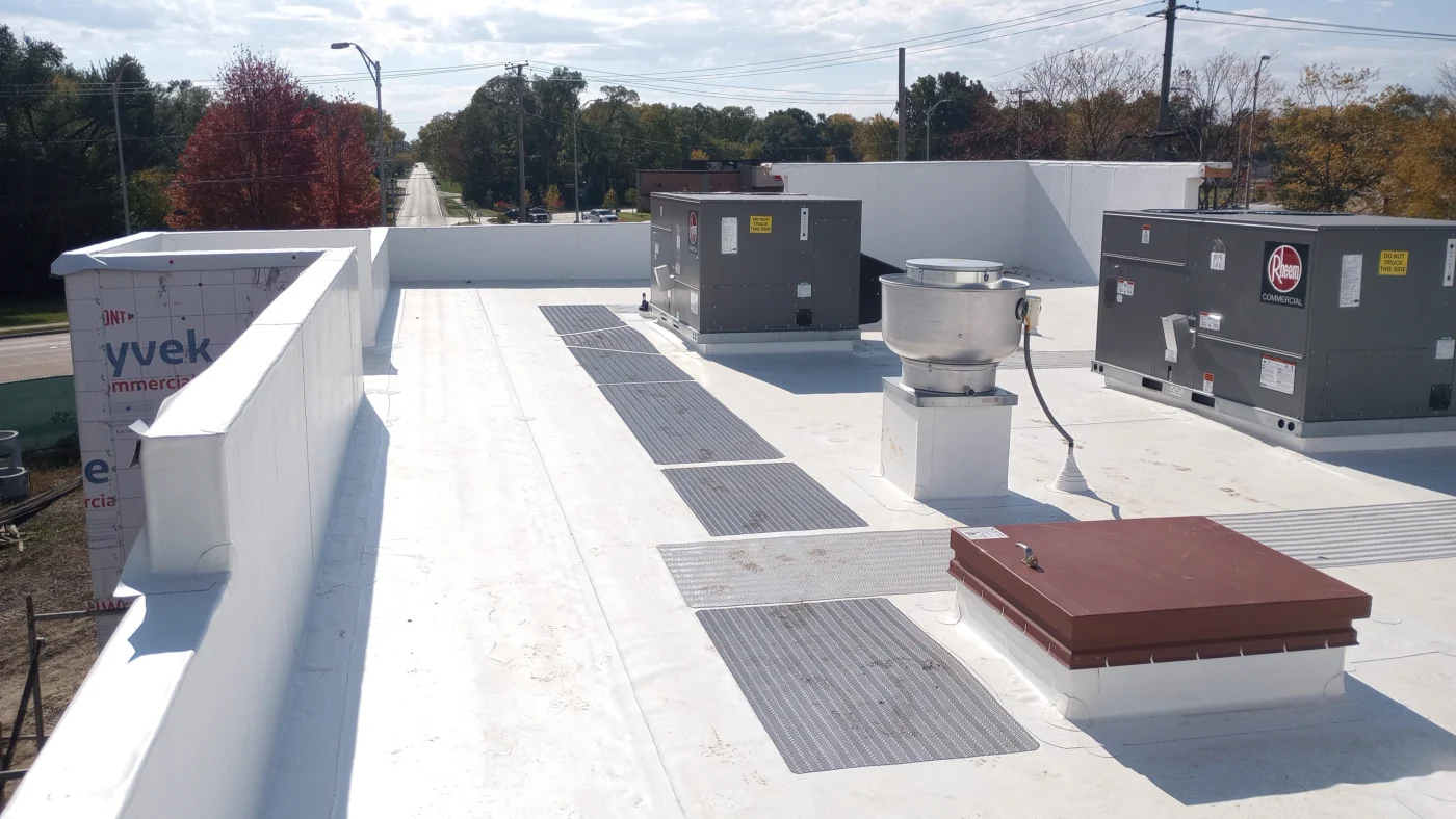 Outstanding Commercial Roofing Contractor | Elgin, IL | Apex Exteriors Inc. White flat commercial roof with membrane surface, rooftop HVAC units, ventilation components, and walkway pads arranged across the building.