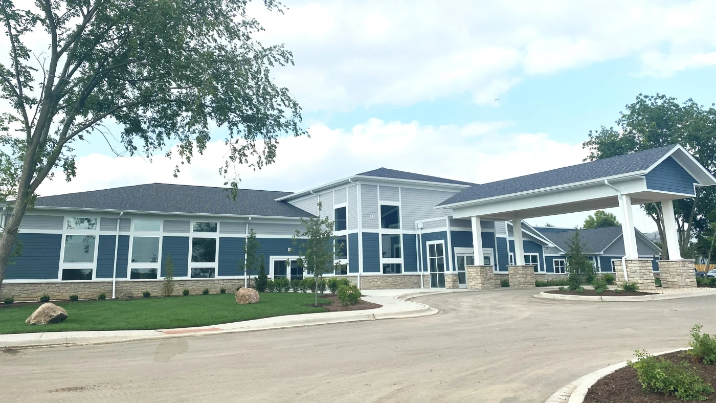 Outstanding Commercial Siding Contractor | Elgin, IL | Apex Exteriors Inc. Contemporary commercial facility with blue horizontal siding, white trim, and stone accents, featuring large windows, a covered entry drive, and landscaped surroundings.