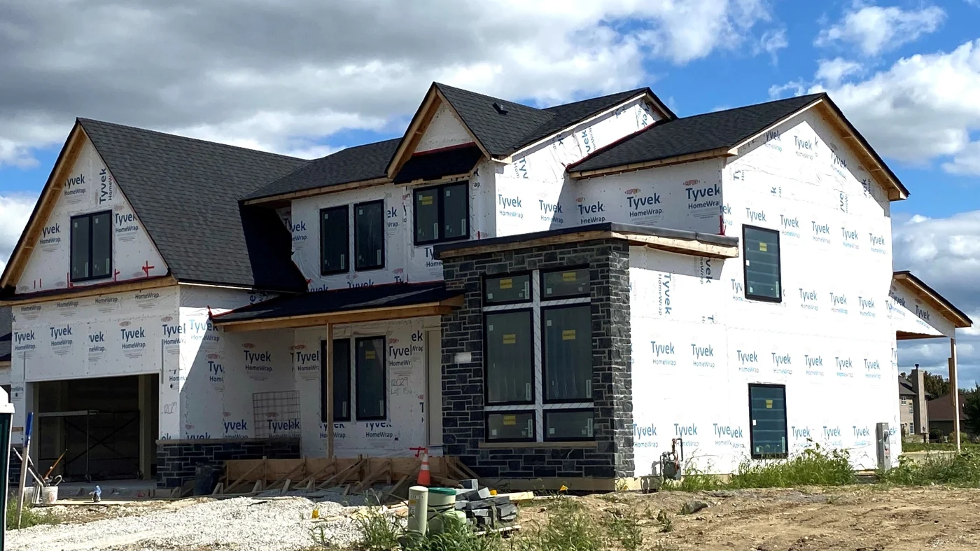 Outstanding New Home Construction | Elgin, IL | Apex Exteriors Inc. New home under construction with dark shingle roof and Tyvek-wrapped exterior, featuring multiple gables and installed windows.