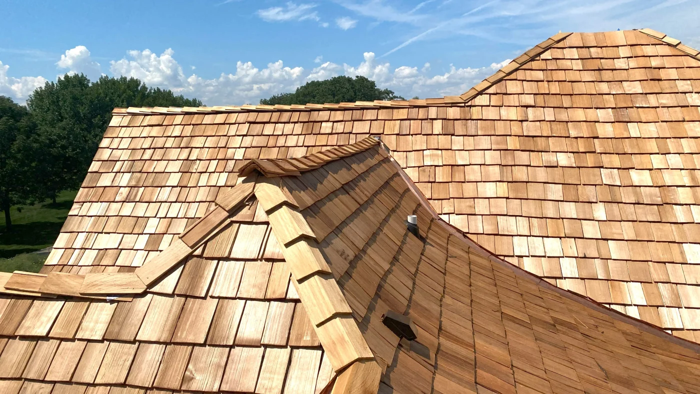Close-up view of a newly installed cedar shake roof showcasing detailed craftsmanship, clean ridge lines, and natural wood variation across multiple roof sections.