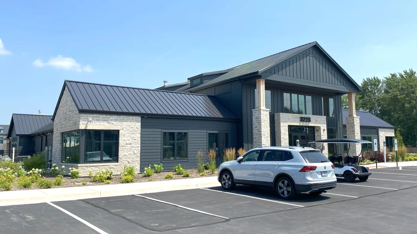 Remarkable Commercial Siding Contractor | Elgin, IL | Apex Exteriors Inc. Modern commercial building with dark vertical siding, stone façade, and metal roofing, featuring large windows and a landscaped entrance with parking area.