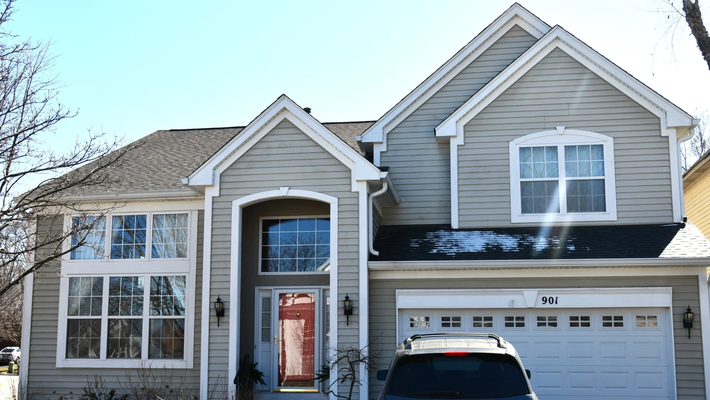 Remarkable Siding Installation | Elgin, IL | Apex Exteriors Inc. Two-story suburban home with light gray siding, white trim, and a dark shingle roof, featuring a red front door and attached garage.