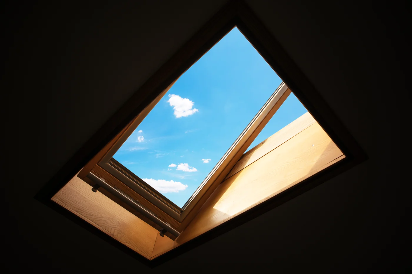The edges of the image are dark, highlighting a large skylight in the center. It opens upward and is famed in medium-colored wood. The blue sky is visible through the glass.